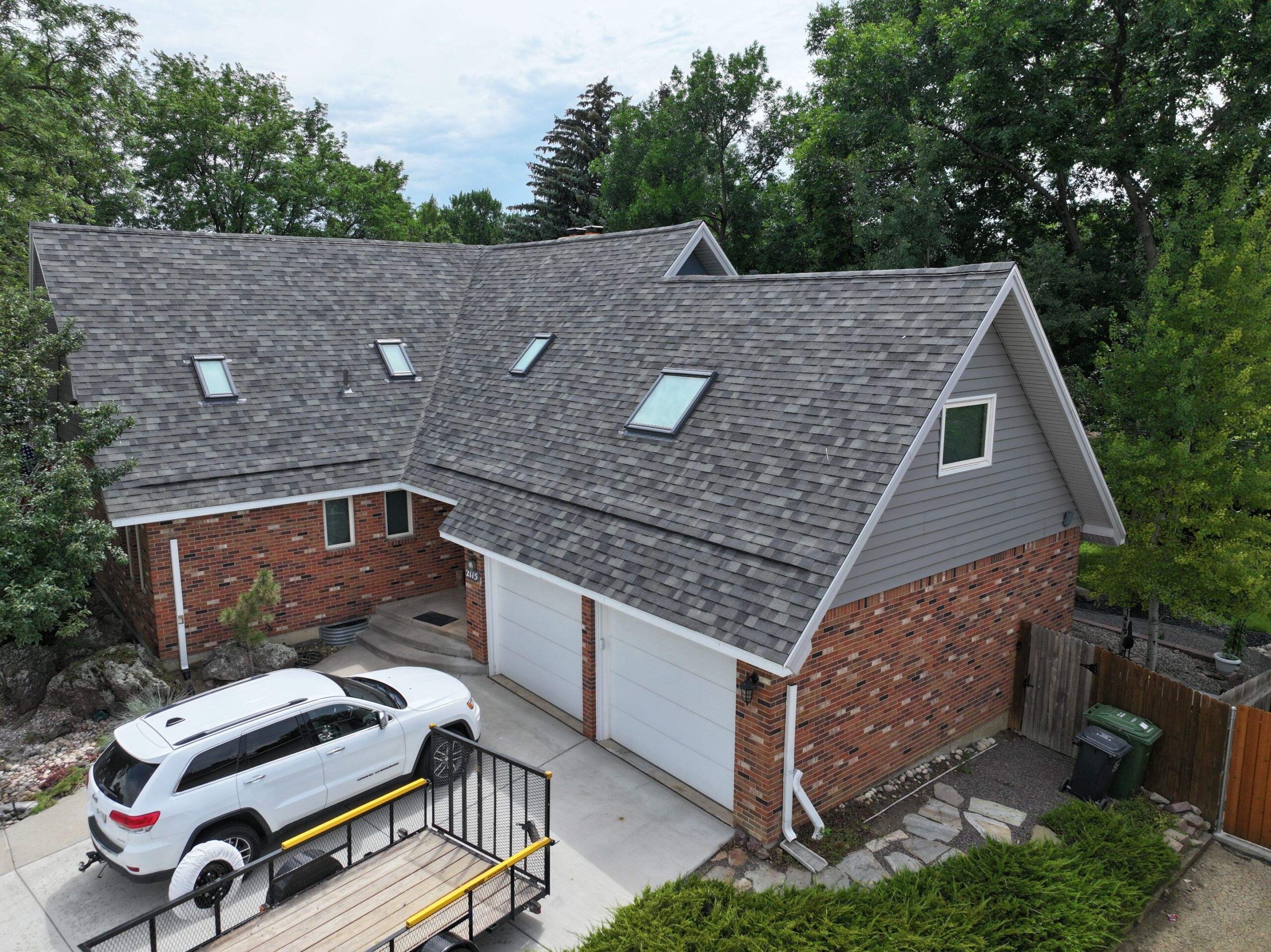 Hail-damaged residential roof restoration showcasing new shingles and skylights, with a white SUV parked in the driveway, emphasizing quality craftsmanship by Sorensen Roofing & Restoration.