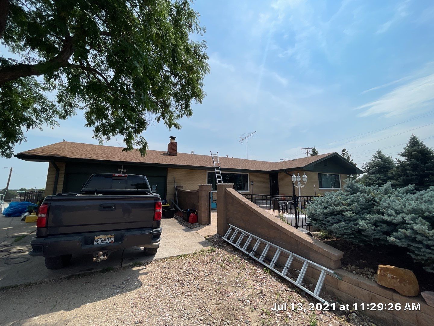 House undergoing inspection for hail damage, with a ladder, truck, and landscaping visible, showcasing the preparation for restoration services by Sorensen Roofing & Restoration.