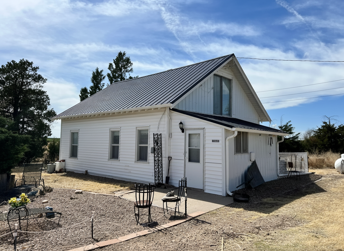 White farmhouse with a newly installed standing seam metal roof, surrounded by a landscaped yard, illustrating hail damage restoration services by Sorensen Roofing & Restoration.